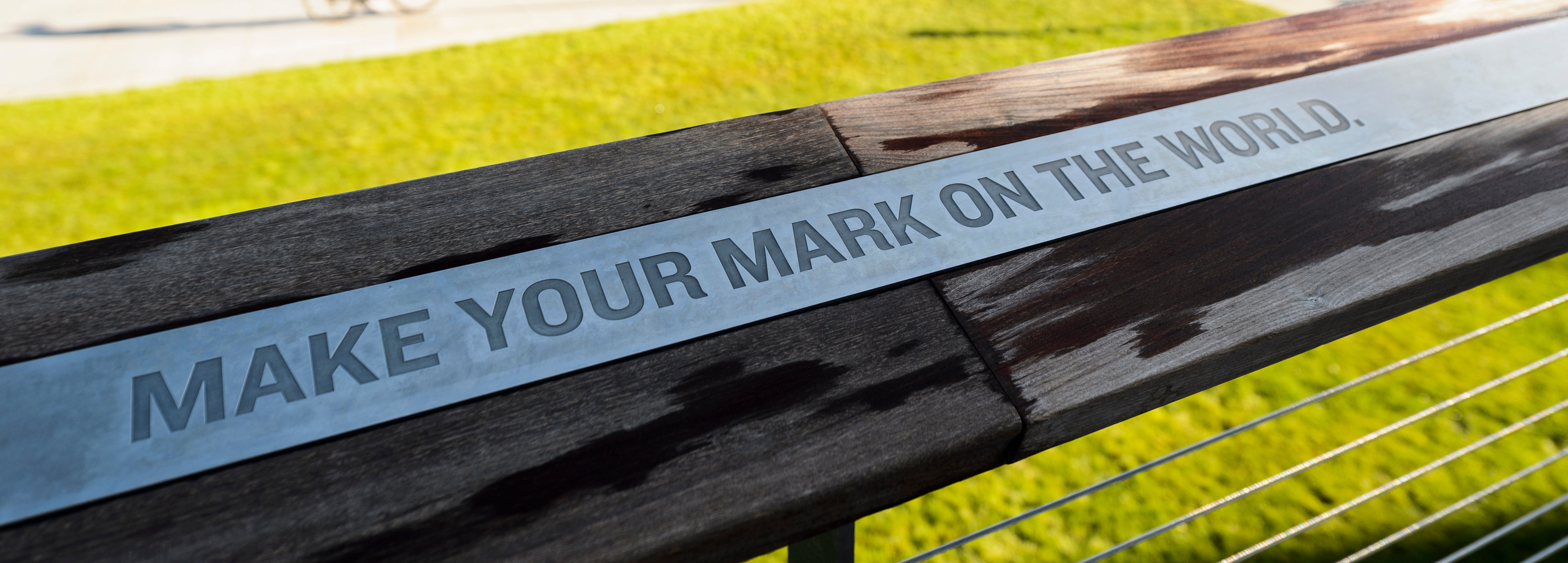 The words "Make Your Mark on the World" are engraved on a silver plaque surrounded by wood. 