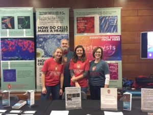 Trainees and faculty posing for a photo with colorful scientific posters behind them. 