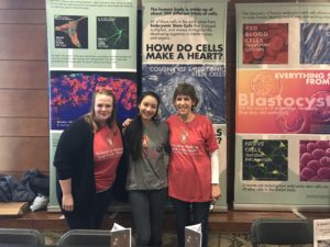 Trainees and faculty posing for a photo with colorful scientific posters behind them. 