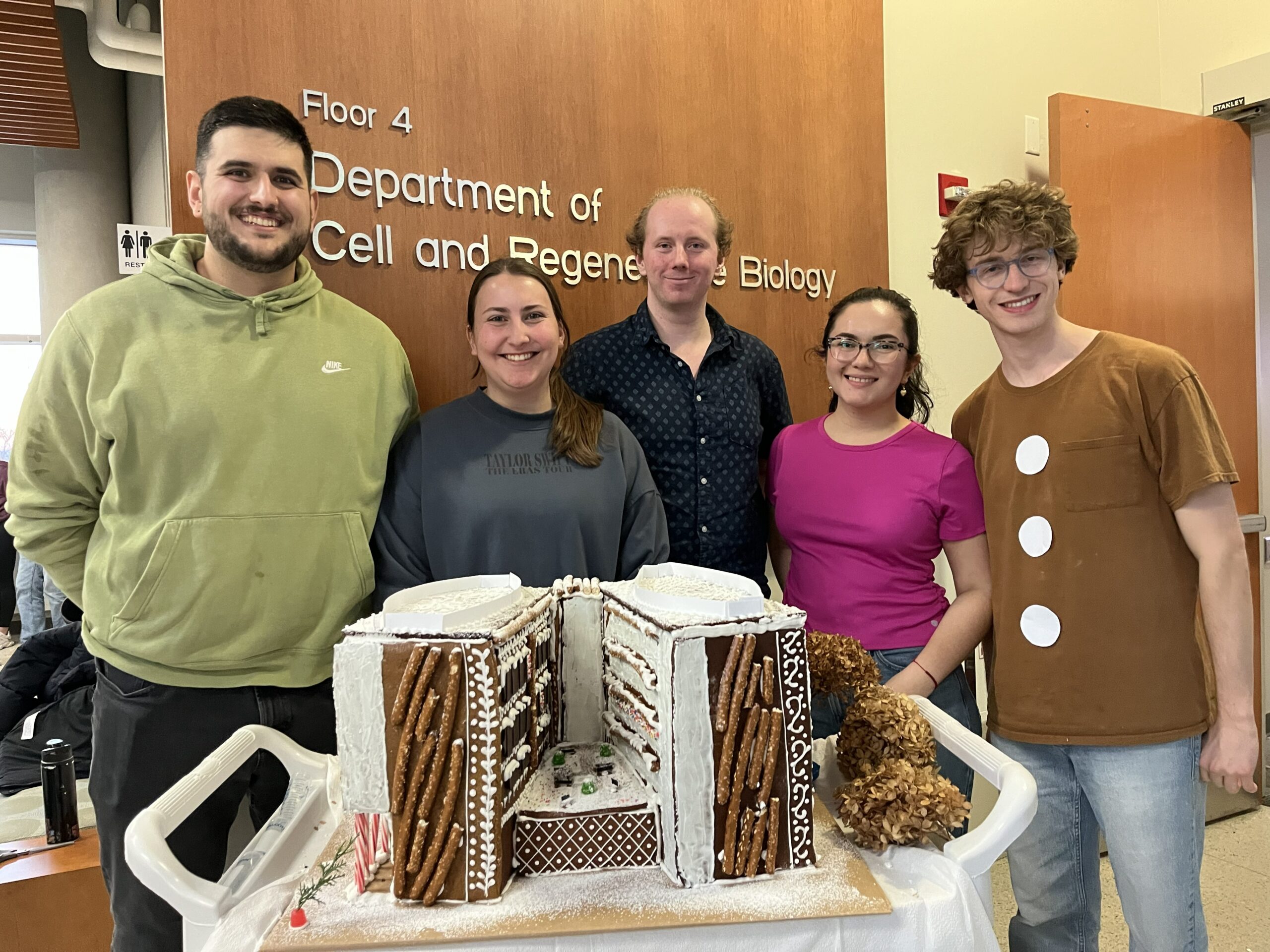 Group of students posing with gingerbread house modeled after Wisconsin Institutes of Medical Research. 